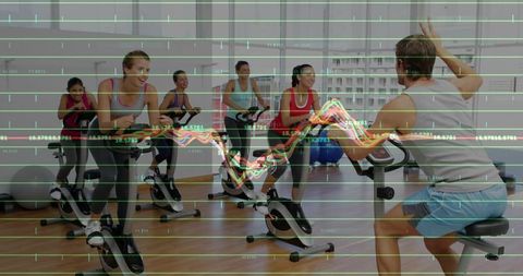 Instructor leading spin class raising hand while cyclists training with analytics overlay