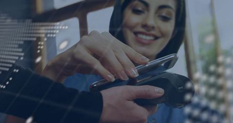 Smiling woman tapping smartphone for contactless payment at checkout terminal