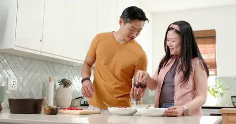 Asian couple cooking together at modern kitchen island preparing fresh salad, smiling