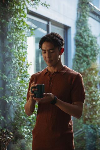 Contemplative asian man standing in sunlit atrium holding green mug