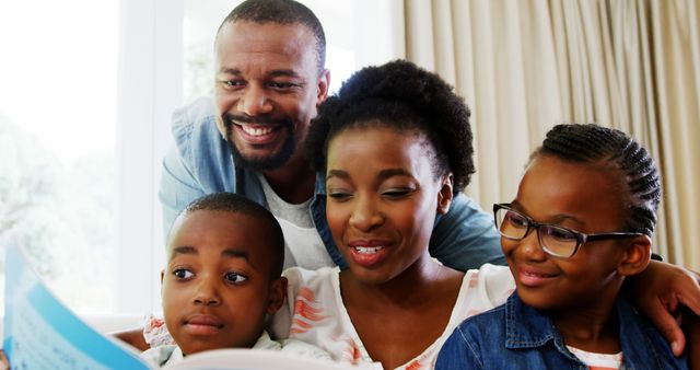 An African American family bonding and enjoying quality time by reading a book together in their living room. The parents and children are engaged and happy, creating a warm and loving atmosphere. Perfect for use in content related to family life, parenting, education, and promoting family engagement.