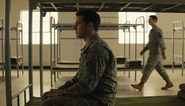 Sitting soldier in camo uniform reflecting in barracks with metal bunks and folded blankets