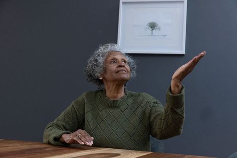 Elderly woman raising hand in thoughtful gesture under art print