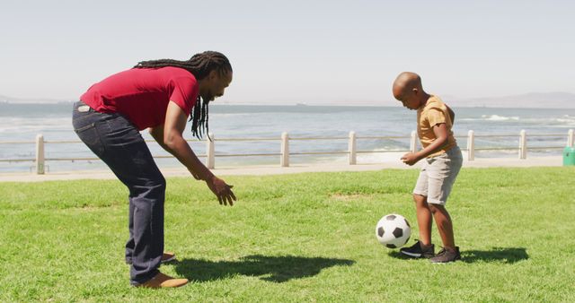 Father and son enjoy playing soccer in a park by the ocean. Ideal for promoting family time, outdoor activities and healthy living. Great for ads, websites, and articles focused on parenting, sportsmanship, and nature.