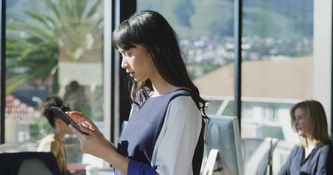 Asian Woman Using Tablet in Sunlit Modern Office