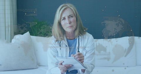 Female doctor writing notes during telehealth consultation with global digital overlay