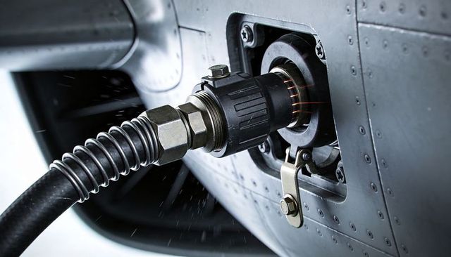 Close-up aircraft refueling nozzle connecting to fuselage fuel port with flexible hose