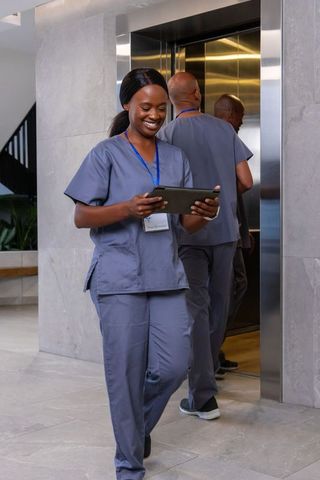 African american nurses walking clinic lobby holding tablet smiling healthcare team