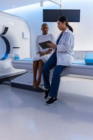 Asian female radiologist consulting patient before ct scan using tablet in radiology suite