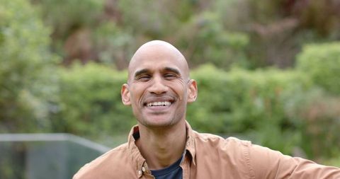 Smiling African American man relaxing in garden wearing tan shirt and dark tee