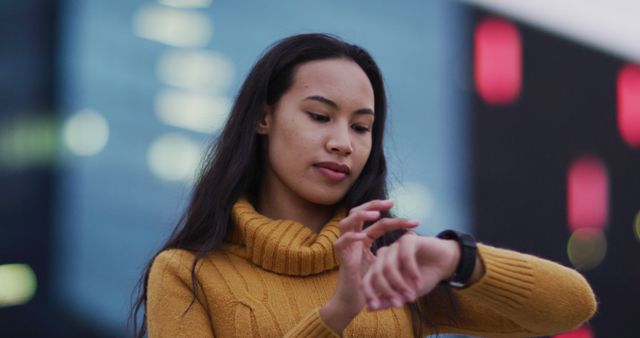 Woman in yellow sweater checking smartwatch in the city. Ideal for illustrating themes of time management, urban living, modern lifestyle, and technology use. Can be used in articles, advertisements, or presentations focusing on fashion, punctuality, and productivity.