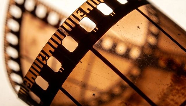 Curling 35mm film strip showing amber frames and sprocket holes backlit by warm light