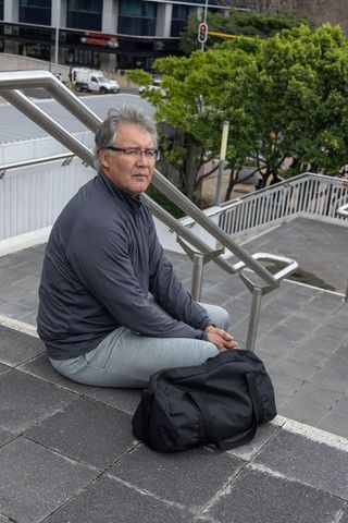 Senior asian man sitting on urban steps with black duffel bag, contemplative moment