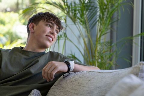 Teen relaxing on sofa wearing smartwatch with indoor plants in sunlit modern living room