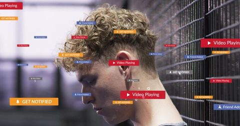 Contemplative young man looking down by metal fence with social media notifications