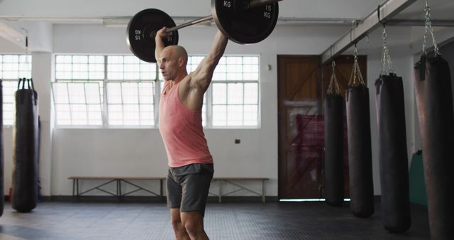Strong athletic man lifting heavy barbell in gymnasium. Perfect for content on fitness routines, strength training, and promoting gym memberships. Useful in articles, advertisements, and social media discussing weightlifting, bodybuilding, and physical fitness challenges.