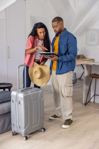 Young couple planning trip in modern loft with suitcase, tablet, itinerary and hat