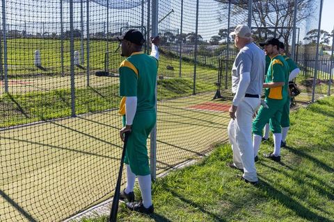 Coach signaling while players preparing at batting cage during outdoor baseball training