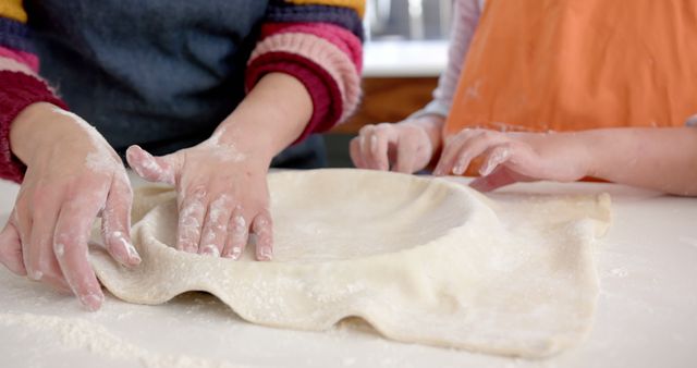 The photo shows a parent and child working together to shape a pie crust on a kitchen counter. Their hands are covered in flour as they collaborate on this baking project. This image is ideal for use in articles, blogs, and advertisements about baking, family activities, parental bonding, and home cooking. It highlights togetherness and the joy of making food at home.
