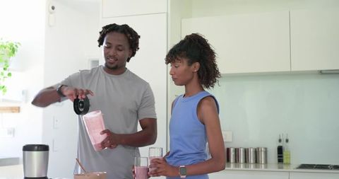 African American couple preparing pink smoothies in modern minimalist bright home kitchen