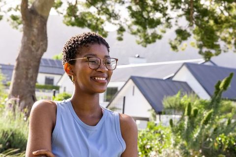 African american woman smiling outdoors in sunlit garden wearing glasses and blue tank top