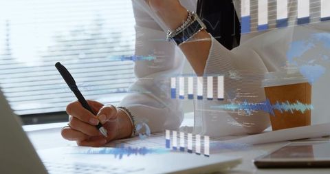 Businesswoman writing and analyzing data reports on office desk with laptop analytics overlay