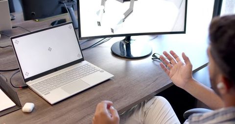 Indian man gesturing while working on 3d design on laptop and monitor at office desk