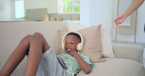 Teen boy relaxing on couch listening to headphones using tablet for learning and play