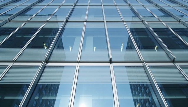 Converging glass curtain wall reflecting urban skyscraper grid, mullions and sun glare