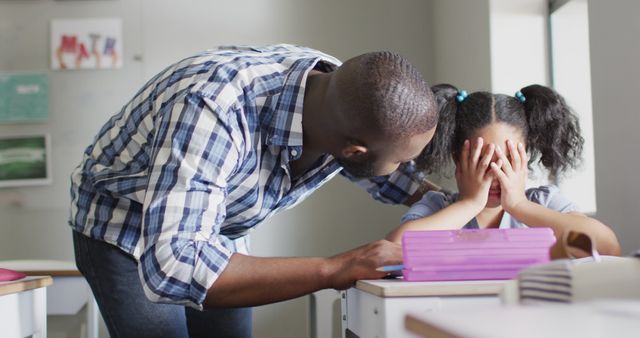 A teacher is kneeling beside a student who is visibly upset with her hands covering her face. This image captures a moment of emotional support and care in an educational setting. It can be used in stories about education, student-teacher relationships, and the importance of emotional support in schools.