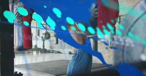 Male boxer punching heavy bag through turquoise plexiglass overlay in urban gym