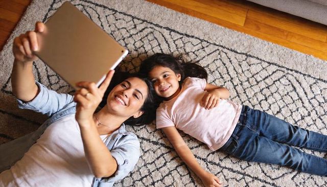 Mother and Daughter Lying on Rug Taking Tablet Selfie, Smiling and Bonding at Home