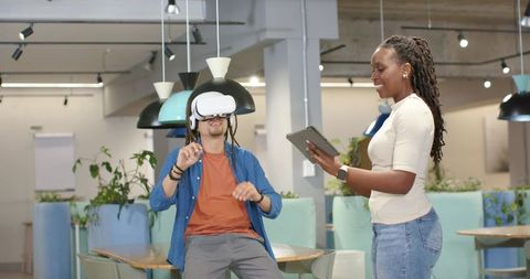 Team testing virtual reality headset in modern coworking lounge, collaborating with tablet