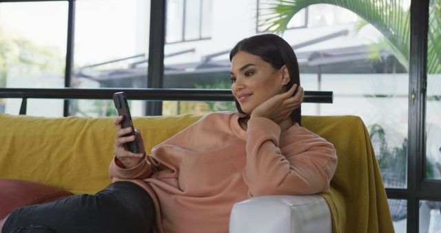 Image of happy biracial woman sitting on sofa and using smartphone - Download Free Stock Photos Pikwizard.com