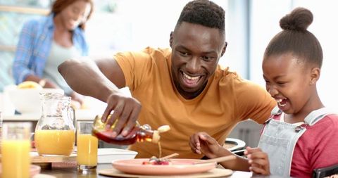 Father Pouring Syrup on Pancakes for Enthusiastic Daughter at Breakfast