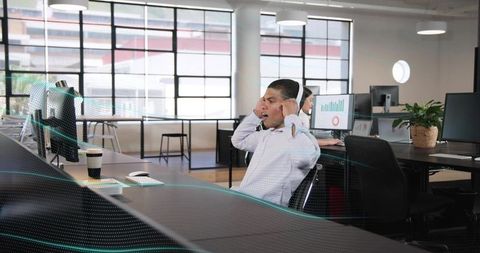 Adjusting Headset in Modern Open-Plan Office with Natural Light and Monitors