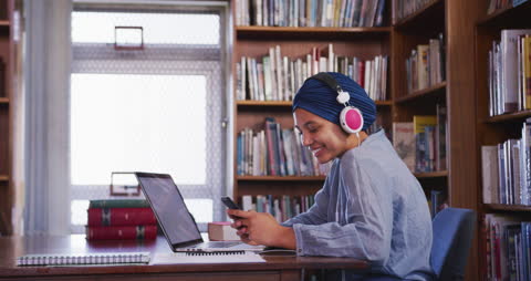 Smiling Student in Hijab Using Smartphone in Library Listening Headphones