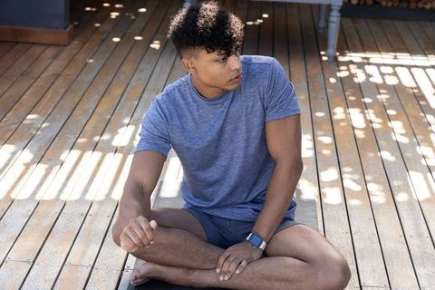 African american man sitting cross-legged on wooden deck wearing smartwatch looking left