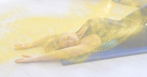 Blonde woman stretching supine on blue yoga mat with golden glow for relaxation and calm