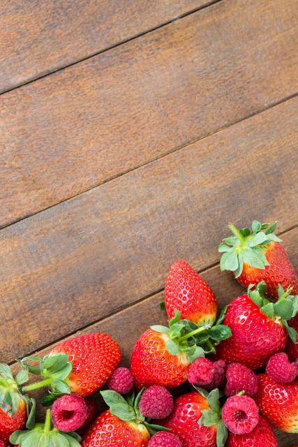 Fresh strawberries and raspberries arranged on a wooden board. Ideal for use in food blogs, healthy eating promotions, recipe books, and advertisements for organic produce. The vibrant colors and natural setting make it perfect for summer-themed content and nutritional guides.