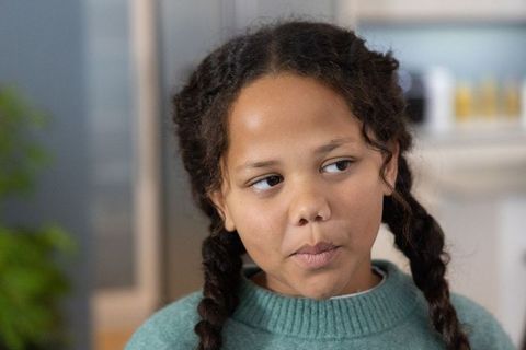 Young girl with braided pigtails wearing teal sweater listening thoughtfully in cozy kitchen