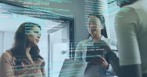 Women collaborating and discussing code with laptop and tablet in modern corporate workspace