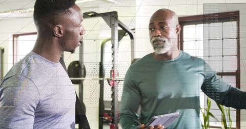 Personal trainer coaching client with tablet in small gym during strength training session
