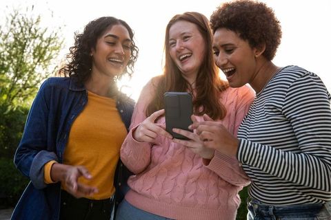 Diverse Female Friends Laughing with Smartphone in Sunlit Garden