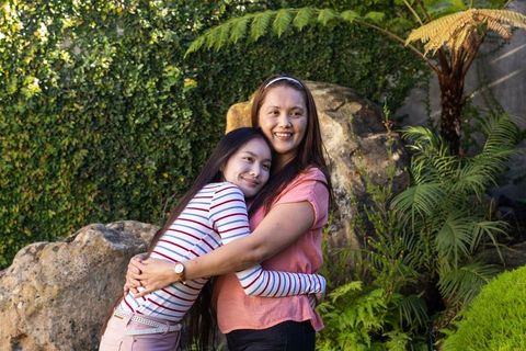 Mother and Daughter Hugging in Garden with Tropical Plants and Rocks