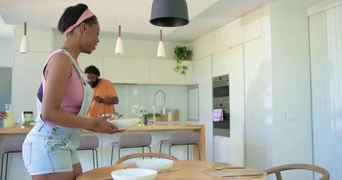 African American family serving dinner in modern bright kitchen with teen carrying bowl