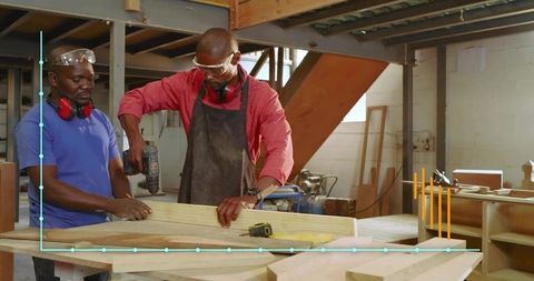 Carpentry team drilling wooden plank in workshop wearing safety goggles and ear protection