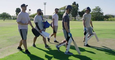 Cricket team walking onto pitch carrying bats and helmets, teammates smiling and chatting