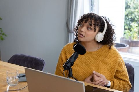 African american woman podcasting at home wearing headphones speaking into microphone