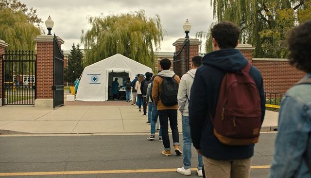 Students waiting in line at campus covid testing tent outside brick university gate